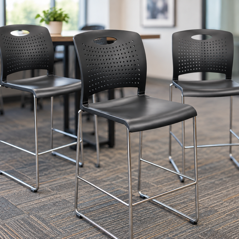 Three black bar stools with perforated backs and chrome legs around a wooden table in a bright office setting