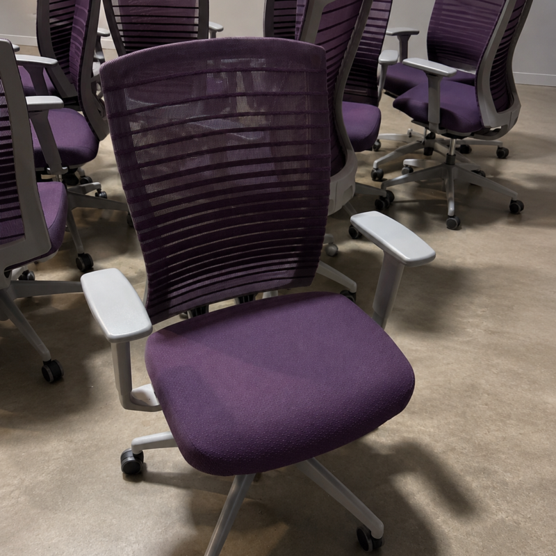 Purple ergonomic office chair with a mesh back and white armrests in a room with several similar chairs arranged in the background.