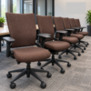 Row of brown upholstered office chairs with wheels lined up along a long meeting table in a bright, modern conference room