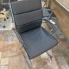 Black leather office chair with a chrome cantilever frame and padded cushions, on a tiled showroom floor
