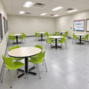 Empty cafeteria or break room with round tables and lime-green chairs arranged around each table in a bright, minimal space.