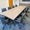 Long wooden conference table surrounded by black rolling chairs in a meeting room, with a cabinet and TV on the back wall.