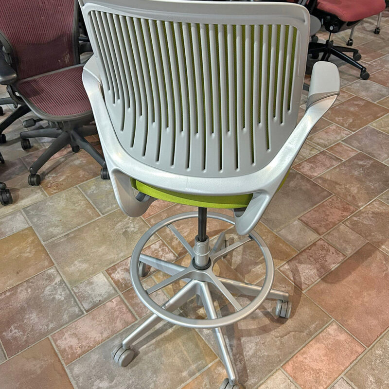 Ergonomic task chair with a white slatted back and lime-green seat, five-wheel base, in a showroom.