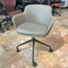 Gray upholstered swivel office chair with curved armrests and a five-wheel base on a tiled showroom floor.