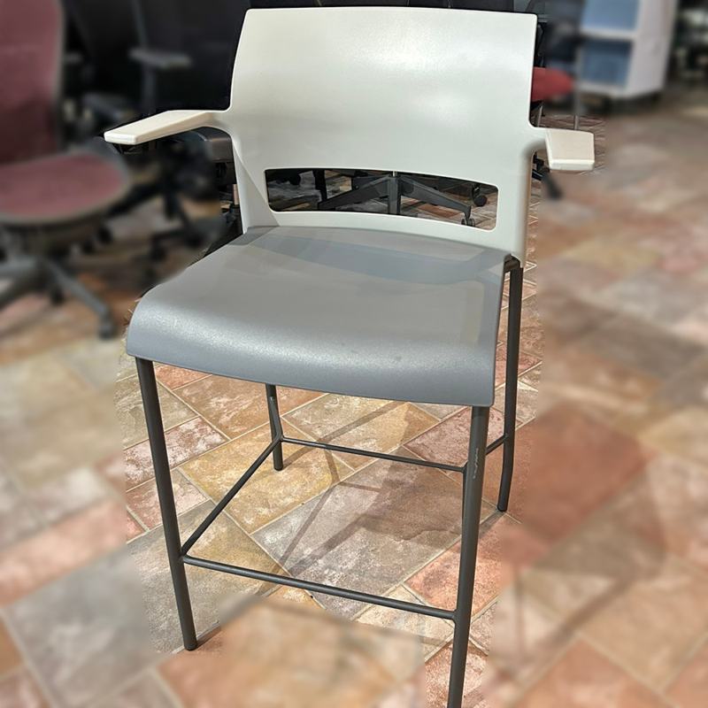 White modern bar stool with a backrest and gray cushioned seat in a showroom on tile flooring.