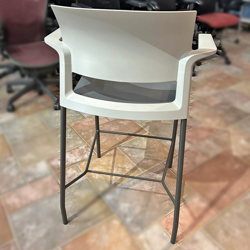 White modern high chair with a curved back and armrests on tall dark metal legs, standing on a tiled floor.